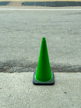 Yeşil bir trafik konisi gün boyunca şehirde bir yolun kenarında duruyor ve etrafında hiç insan yok..