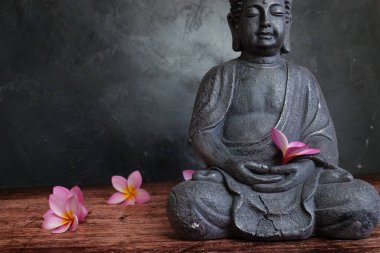Koyu arkaplanda Frangipani çiçekleri olan Buda heykeli