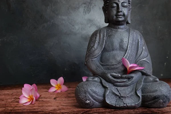 Koyu arkaplanda Frangipani çiçekleri olan Buda heykeli