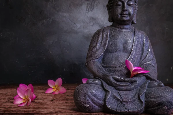 Buddha statue with frangipani flowers on a dark background — Stock Photo, Image