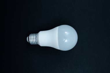 Beyaz plastik bir kubbe ve metal vida tabanlı LED ampul, koyu siyah arka planda yatay olarak sunuluyor. Gücü ve yeniliği sembolize eder. Resmin ortasında sunuluyor.