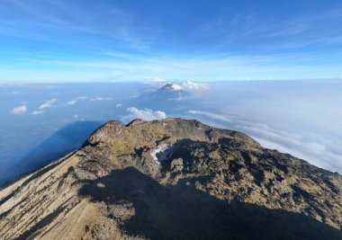 Yukarıdan çekilen manzara, dağlık bir arazinin yer aldığı geniş bir manzarayı gözler önüne seriyor. Açık mavi gökyüzü ve seyrek bulutlar çarpıcı bir zemin sağlar, yükseltilmiş perspektifin doğal güzelliğini arttırır..
