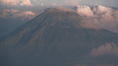 Bulutların üzerinde yükselen devasa bir dağın manzarası. Dağ sisli bir sis ile çevrilidir. Güneş bulutlardan ve gökyüzünden yansıyor, doğadaki doğal manzara..