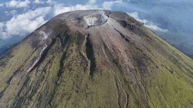 Hava manzarası belirgin krateri, yemyeşil bitki örtüsü ve engebeli volkanik kaya oluşumlarıyla görkemli bir volkan sergiliyor. Seyahat, doğa, macera temaları için ideal