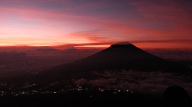 Bu nefes kesici manzarayla şafağın dingin güzelliğini deneyimleyin. Bir dağ silueti, dramatik bir gündoğumu ve bulutlarla birlikte barış ve güzellik sunuyor. Seyahat için ideal, doğa.