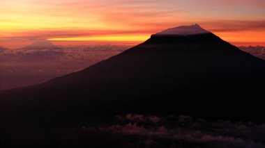 Canlı bir günbatımı gökyüzüne karşı volkan silueti içeren dramatik bir çekim, macera ve sükunet atmosferi yaratır. Seyahat, doğa ve ilham için mükemmel.
