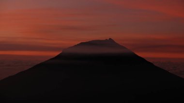 Gün doğumunda canlı kırmızı bir gökyüzünün altındaki bir dağın çarpıcı silueti. Bu macera, doğa ve sükuneti yakalar. Seyahat, kaçış ve açık hava kavramları için harika.