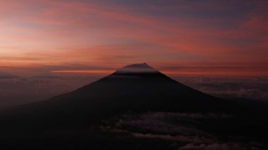 Canlı, renkli bir günbatımı gökyüzüne karşı yükselen bir dağın siluetini barındıran nefes kesici bir manzara. Huzuru ve merakı çağrıştırıyor. Seyahat, doğa ya da ilham verici konular için ideal