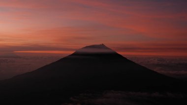Canlı bir günbatımına karşı siluetlenmiş volkanik bir tepenin hayranlık uyandıran güzelliğini yakalayın. Bulutlar bu manzaraya dram katıyor. Seyahat, doğa veya ilham verici temalar için kullan