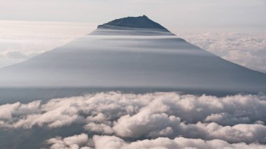 Sakin bir dağ kalın bulutları delip geçer, rüya gibi ve ilham verici bir manzara yaratır. Meydan okumayı, zaferi, macerayı ve sükuneti sembolize et. Seyahat, doğa ve motivasyon temaları için ideal