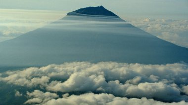 Havadan bakıldığında dağ zirvesinin bulutlarla çevrili olduğu görülüyor. Doğa ve manzara dingin ve ilham verici bir ortam yaratır. Seyahat, doğa ve ilham verici bağlamlar için mükemmel.