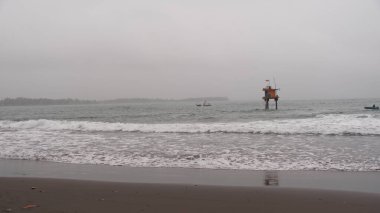 Sisli bir plajın sükunetini bu görüntüyle yakalayın. Denizde bir kule ve uzak tekneler gösteriyor, seyahat için mükemmel, sahil temaları, doğa terfisi, ve barışçıl ruh hali. Web siteleri, broşürler ve reklam kullanımı için ideal