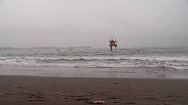 Huzurlu ama kasvetli bir deniz manzarası kumlu bir sahilde okyanus dalgalarının kırılışını gösteriyor. Uzak bir yapı kalelerin üzerinde duruyor, yalnızlığı çağrıştırıyor. Sükunet, esneklik veya izolasyon aktarımı için ideal