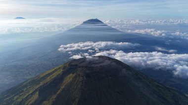 Havadan bakıldığında bulutlarla çevrili volkanik dağ zirveleri görülüyor. Sis ruhani bir kalite ekler. Seyahat, doğa, macera teması için ideal. Barışı, korkuyu ve merakı çağrıştırıyor. Yüksek kalite çözünürlük ve berraklık