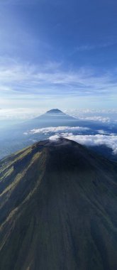 Havadan çekilen bir görüntüde bulutların arasından geçen iki dağ, korku ve sükunet hissi yaratıyor. Seyahat, doğa, macera ya da ilham verici içerik için mükemmel