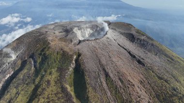 Hava görüntüsü bir yanardağı yakalıyor. Gri ve kahverengi yamaçlar ve dumanı tüten krater. Yer bilimi ve coğrafya için görkemli bir dağ tepesi. Doğa ve seyahat kavramları için kullan