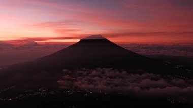 Çarpıcı bir gün doğumu, siluetli bir dağın tepesinde gökyüzünü kızgın renklerle boyar. Seyahat, macera ya da ilham verici içerik için ideal, merak duygusu yaratmak için. Arka plan için mükemmel.