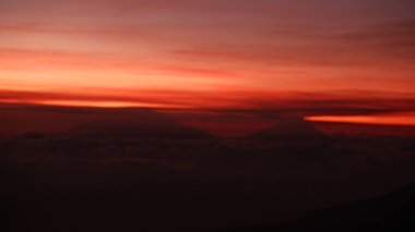 Dağların tepelerinde bulutlarla örtülü çarpıcı bir gün doğumu. Kızıl ve turuncu gökyüzü dramatik bir manzara çizer, seyahat, macera ve ruhani temalar için mükemmeldir. Huzurlu ama güçlü