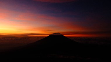 Çarpıcı bir dağ silueti canlı bir gündoğumu gökyüzüne karşı duruyor. Görüntü huzuru, macerayı ve doğanın güzelliğini yansıtıyor. Seyahat ve açık hava temaları için mükemmel