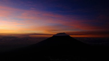 Sakin bir dağ silueti renkli bir günbatımına karşı duruyor. Bu görüntü huzuru ve huzuru çağrıştırıyor. Seyahat, doğa ve ilham verici içerik için mükemmel. Arkaplan için kullan