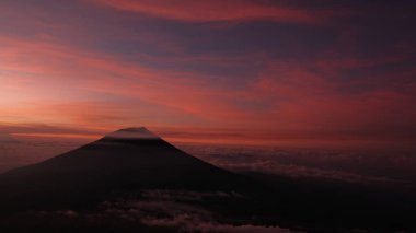 Canlı bir gündoğumu gökyüzüne karşı bir dağ siluetinin nefes kesici görüntüsü. Huzur ve ilhamı çağrıştırıyor. Seyahat, doğa ya da ilham verici temalar için mükemmel. Bulut manzarası görünümü