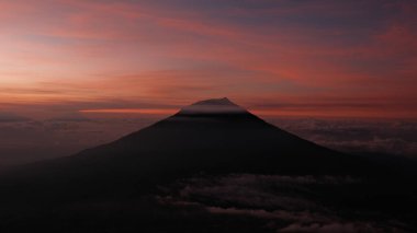 Canlı, renkli bir günbatımı gökyüzüne karşı yükselen bir dağın siluetini barındıran nefes kesici bir manzara. Huzuru ve merakı çağrıştırıyor. Seyahat, doğa ya da ilham verici konular için ideal