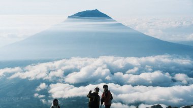 Yürüyüşçüler bulutlarla çevrili bir dağ zirvesinden çarpıcı bir manzaranın keyfini çıkarırlar. Görkemli bir dağ sırası bulutların üzerinde yükselir, sakin bir atmosfer, seyahat, macera yaratır.