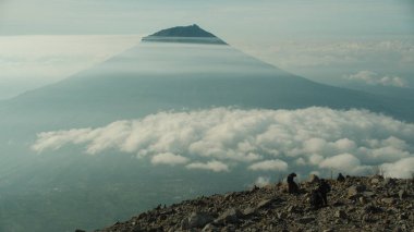 Huzurlu bir manzarada görkemli bir dağ zirvesi kabarık bulutlar denizinin üzerinde yükseliyor. Volkanik manzara, macera yolculuğu ve kaçış konsepti. Seyahat ve doğa satmak için kullanılabilir.