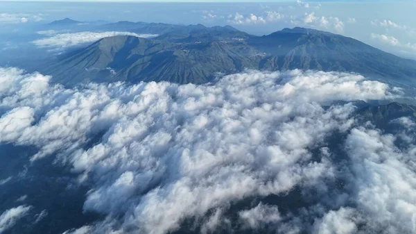 Tepeden çekilen fotoğraf bulutlu bir battaniyeden yükselen dağları temsil ediyor. Zirveler gökyüzüne yükselir. Görüntü huzuru ve macerayı çağrıştırıyor. Seyahat, doğa ve ilham için ideal. Manzara