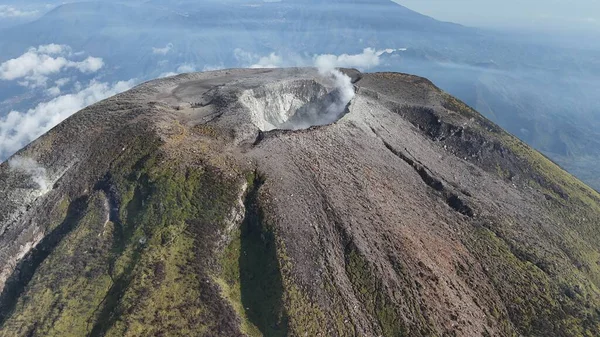 Hava görüntüsü bir yanardağı yakalıyor. Gri ve kahverengi yamaçlar ve dumanı tüten krater. Yer bilimi ve coğrafya için görkemli bir dağ tepesi. Doğa ve seyahat kavramları için kullan