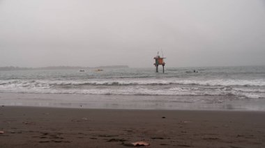 Huzurlu ama kasvetli bir deniz manzarası kumlu bir sahilde okyanus dalgalarının kırılışını gösteriyor. Uzak bir yapı kalelerin üzerinde duruyor, yalnızlığı çağrıştırıyor. Sükunet, esneklik veya izolasyon aktarımı için ideal