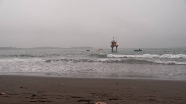 Sakin ama kasvetli bir deniz manzarası. Kıyıya yakın, bulutlu bir gökyüzünün altında, yumuşak dalgaların arasında bir açık deniz platformu. Kıyı temalarını, deniz sorunlarını veya yalnızlığı resmetmek için ideal