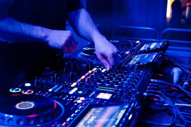 Bir DJ, karanlık bir gece kulübünde profesyonel ses ekipmanlarının parçalarını ustalıkla karıştırarak heyecan verici bir atmosfer yaratıyor..