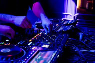 Profesyonel DJ, canlı bir gece kulübü ortamında gelişmiş ses ekipmanları üzerinde ustalıkla şarkı karıştırıyor.