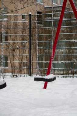 Kışın terk edilmiş oyun parkı. Karla kaplı salıncaklar ve donmuş manzarayla.