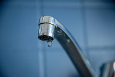 Damlayan musluğun mavi fayanslı bir duvara yakın çekimi, sıhhi tesisat sorununu vurguluyor.