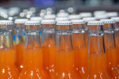 Portakallı gazozla dolu sıra sıra sıra cam şişeler üretim hattında veya depoda, bir ferahlatıcı ve ticari üretim hissini iletiyor