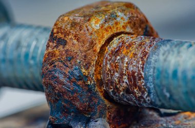 Paslı metal cıvata ve somun yakın plan şiddetli aşınmayı ve demirde çürümeyi gösteriyor, yıpranmış dokuyu ve oksidasyonun canlı turuncu-kahverengi renklerini vurguluyor.