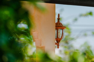 Yumuşak yeşil bokeh ile çevrili dokulu bir duvara monte edilmiş klasik tip lamba, dışarıda huzurlu bir ortam yaratıyor. Fotoğraf, üretken ai yok