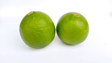 Beyaz zemin üzerinde iki taze yeşil limon, C vitamini ve antioksidan açısından zengin tropikal narenciye meyvesi.