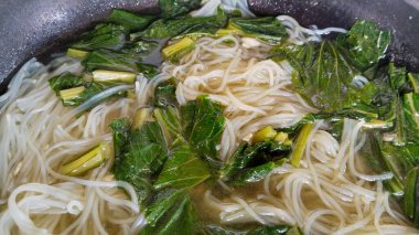 Yeşil yapraklı sebzelerle pişirilmiş erişteli pirinç çorbası.