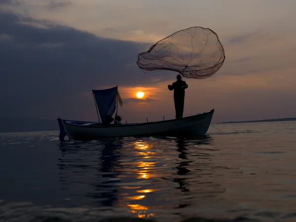Рибалка кинув сітку в озеро під час заходу сонця — стокове фото