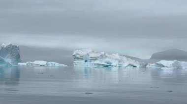 Grönland Kutup Bölgesi 'nin nefes kesici güzelliğini tecrübe edin. Devasa buzulların ve yükselen buzdağlarının el değmemiş turkuaz sularda zarafetle yüzdüğü yer. Bu sakin ama dramatik sahne ham gücü vurguluyor.