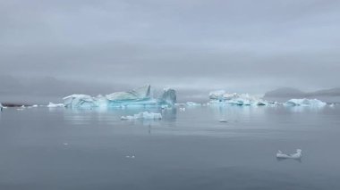 Grönland Kutup Bölgesi 'nin nefes kesici güzelliğini tecrübe edin. Devasa buzulların ve yükselen buzdağlarının el değmemiş turkuaz sularda zarafetle yüzdüğü yer. Bu sakin ama dramatik sahne ham gücü vurguluyor.