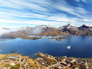 Doğu Grönland 'daki en büyük kasaba olan Tasiilaq' ın atmosfer manzarası. Alçak bulutlar, koyu mavi fiyortlara, buzdağlarına ve renkli yerleşimlere bakan sivri dağ tepelerini sarıyor. Kuzey Kutbu seyahatleri ya da doğa belgeselleri için mükemmel bir kurgu..