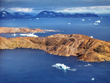 Doğu Grönland 'daki en büyük kasaba olan Tasiilaq' ın atmosfer manzarası. Alçak bulutlar, koyu mavi fiyortlara, buzdağlarına ve renkli yerleşimlere bakan sivri dağ tepelerini sarıyor. Kuzey Kutbu seyahatleri ya da doğa belgeselleri için mükemmel bir kurgu..