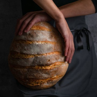 Fırıncı kadın elinde buğday ekmeği tutuyor.