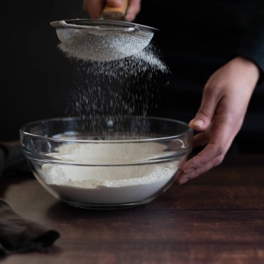 Ekin manzaralı kadın elleri süzgeçten un geçiriyor.