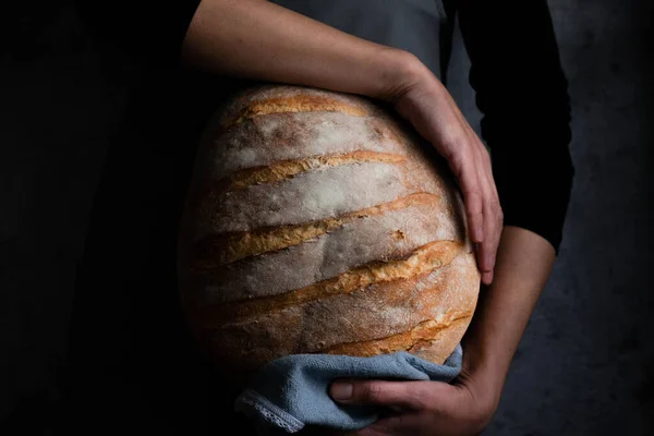 Fırıncı kadın elinde buğday ekmeği tutuyor.