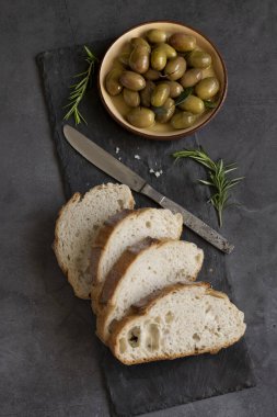 İtalyan dilimlenmiş ciabatta ekmeği otlarla doğranmış, ekstra bakire yağı ve koyu grunge arka planda marine edilmiş zeytinler.